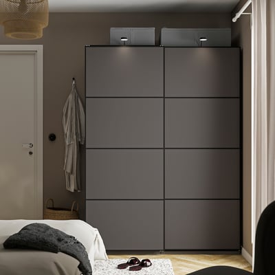 Modern dark grey PAX wardrobe beside bed with white blanket, basket, coat rack, and frosted door.
