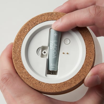 Hands holding a battery-operated lamp with a cork base and glass dome.