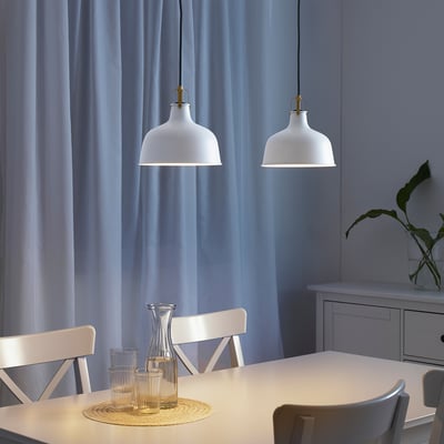 Three hanging lamps illuminate a dining table with glasses and a vase, casting warm light.