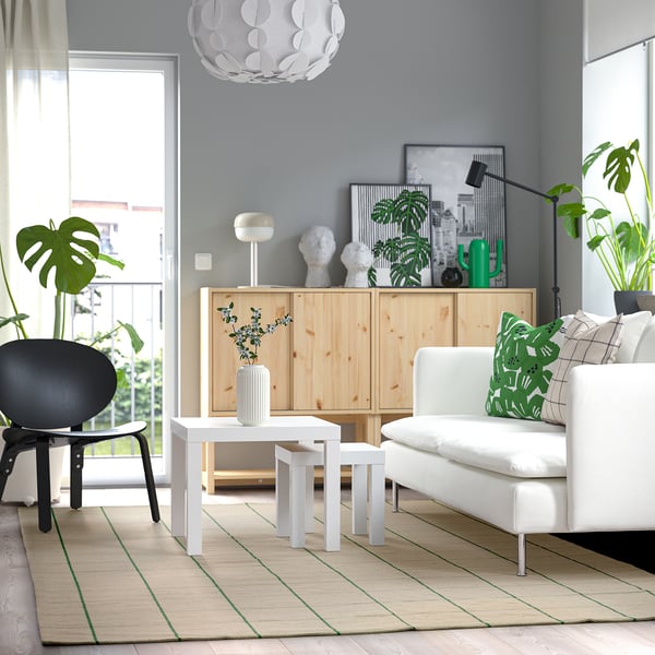 Modern living room with white rug, coffee table, couch, and cabinet. Greenery and natural light.