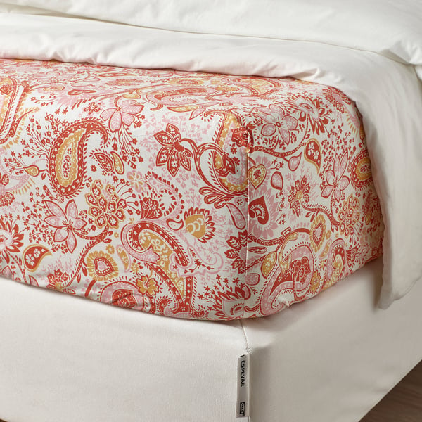 A bed with a fitted sheet featuring a vibrant red paisley pattern, showing elastic edges fitting the mattress.