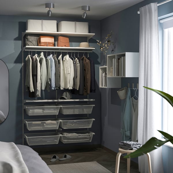 Organised closet with shelves, hangers, baskets, and storage bins. Dark blue walls with white curtains. Plants and storage racks visible.