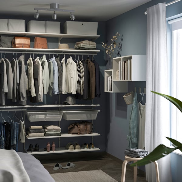 Organised closet with clothes, shelves, stool, plant, ceiling spotlight.