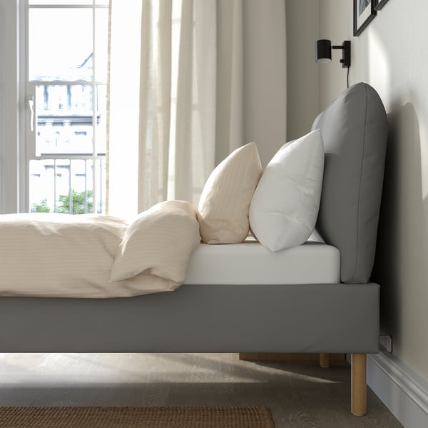 Modern bedroom with upholstered bed frame, sloped headboard, white pillows, and natural daylight filtering through curtains.