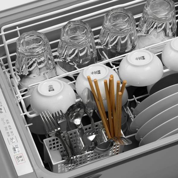 Open dishwasher showing glasses, bowls, cutlery, and chopsticks arranged on racks, ready for washing.