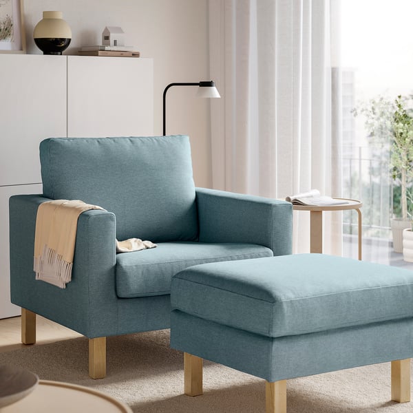 Light blue chair & ottoman set, wooden legs, near window with sheer curtains, cosy minimalist room.