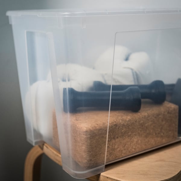 Clear plastic storage box filled with sponges, scrubbers, and black items, resting on a wooden surface.