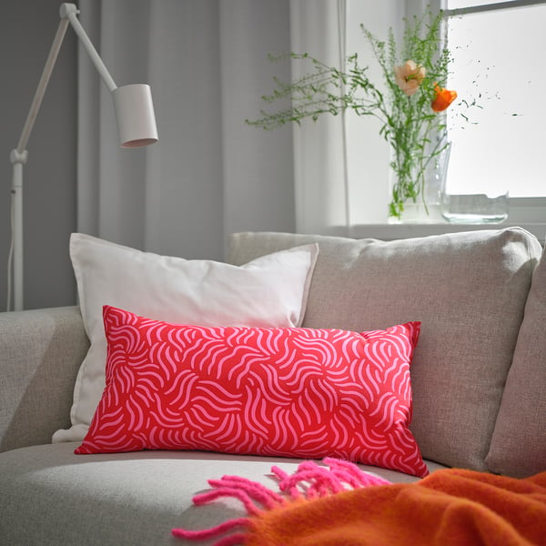 Bright red SANDMOTT cushion on grey couch, patterned, large, soft, near flowers.