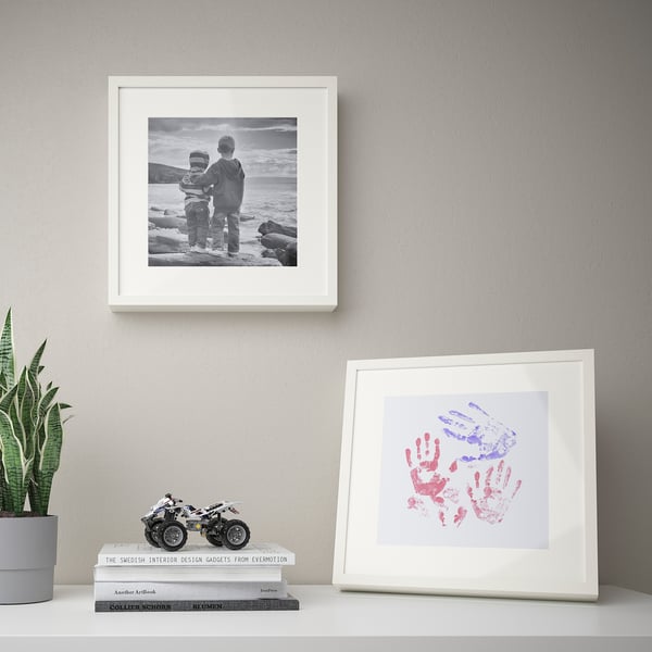 Two framed memories: black & white kids by sea, colourful handprints below. Plant & books complete cosy wall.