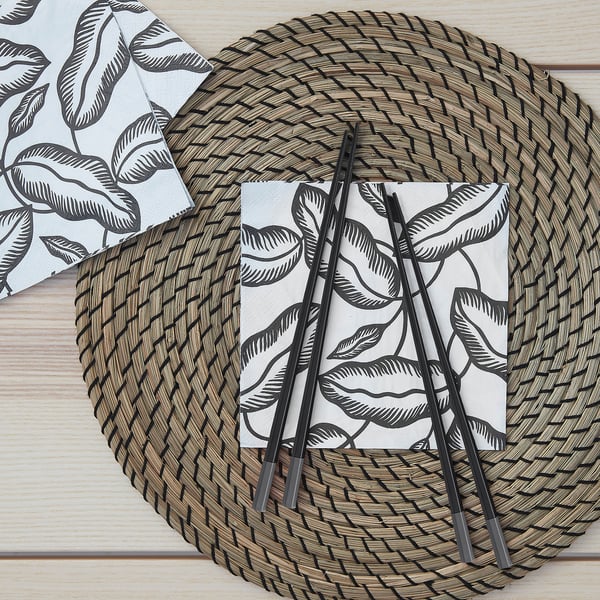 A pair of hexagonal, anti-slip chopsticks rests on a woven place mat with a leaf-patterned napkin.