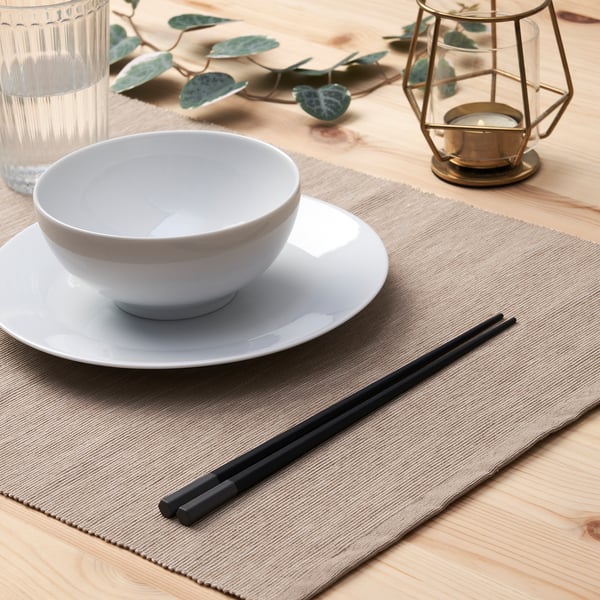 White bowl on plate with chopsticks, lantern, and greenery.