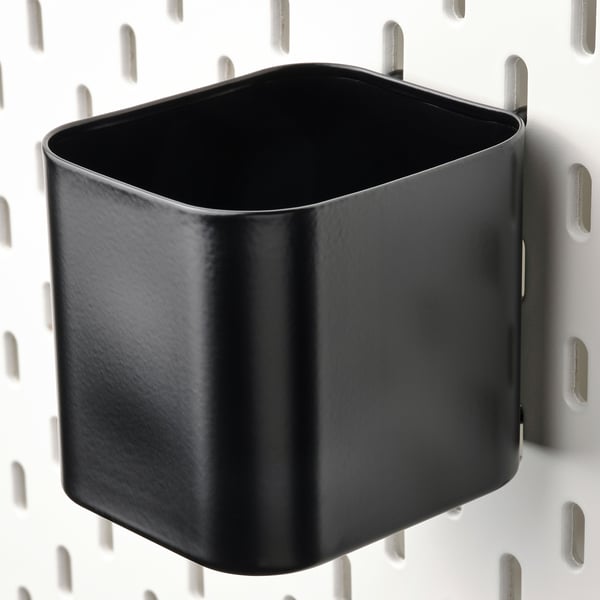 Black metal storage cup attached to a pegboard for organised storage.