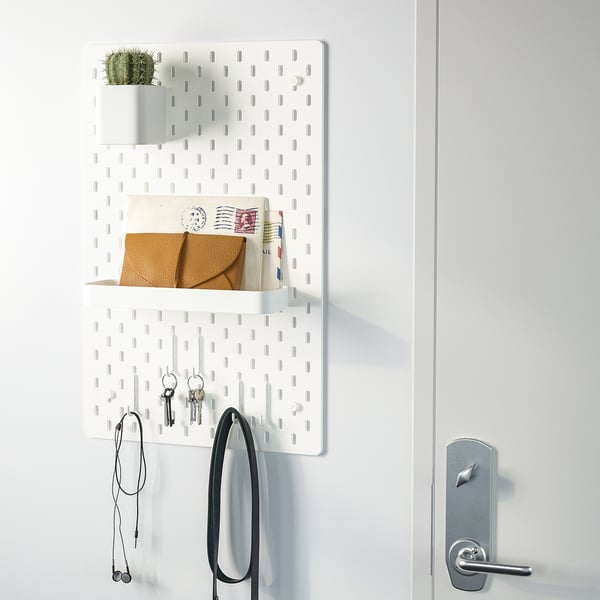 White wall organiser with shelves, hooks, and plant holder near a door.