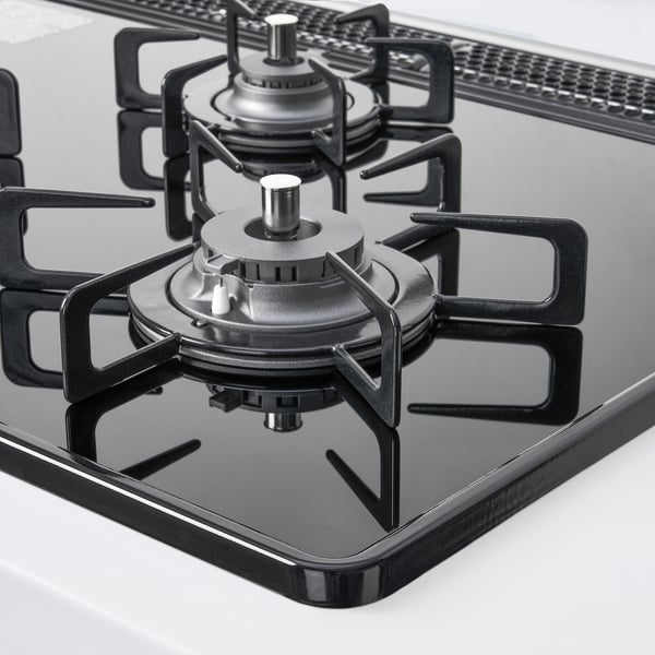 Modern gas stove with four burners and cast iron supports on a glass surface.