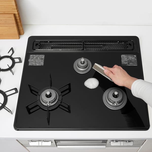 Cleaning a black stovetop with a sponge and detergent.