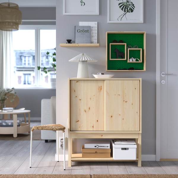 Natural wood SKOGSMOSAIK shelf with 2 inner shelves, boxes, lamp, and bench between art and door.