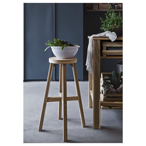 SKOGSTA stool in natural acacia wood with round seat. Decorative bowl with plant on top.