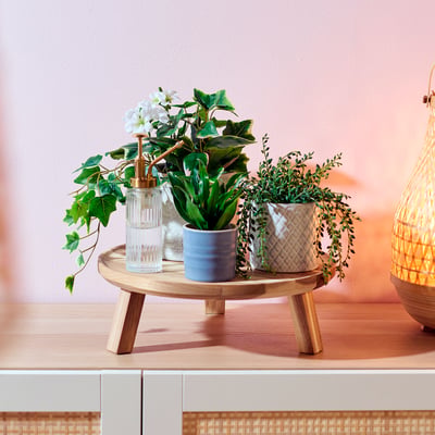 Wooden plant stand with glass and ceramic pots holding greenery and flowers.