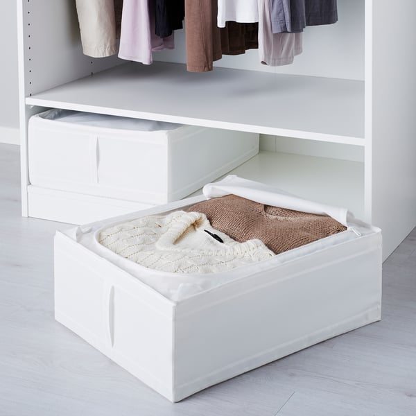 White under-bed storage box with clothes, part of IKEAs SKUBB series for dust protection and air circulation.