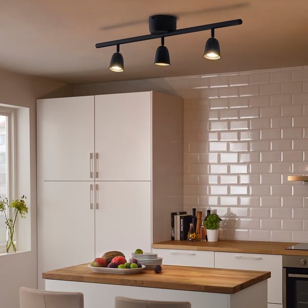 Modern kitchen with black ceiling light illuminating wooden counter, white cabinets, pink tiles, and chairs.