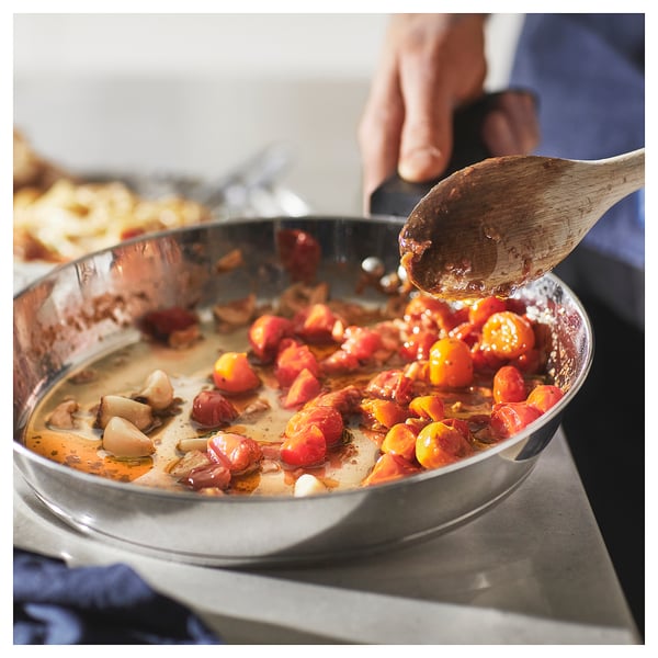 A person stirs tomatoes and garlic in a stainless-steel SLÄTROCKA pan.