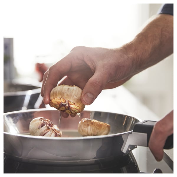 Person placing garlic in stainless steel slotted pan with removable handle.