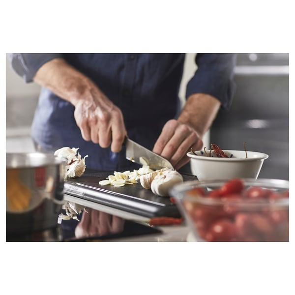Person slicing garlic on cutting board with knife, bowl of tomatoes nearby.