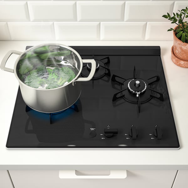 Gas stove with three burners; one in use for boiling vegetables on a modern kitchen countertop.