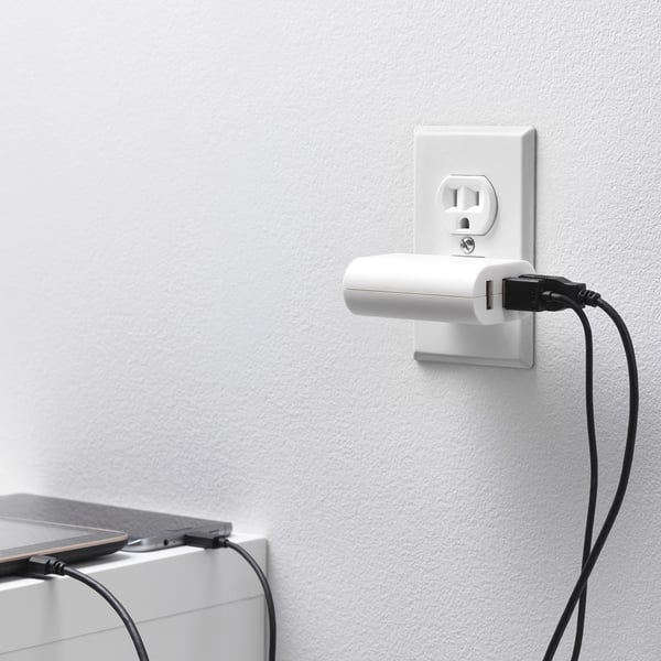 A compact, wall-mounted charger with three usb ports, plugged into an outlet, charging multiple devices.