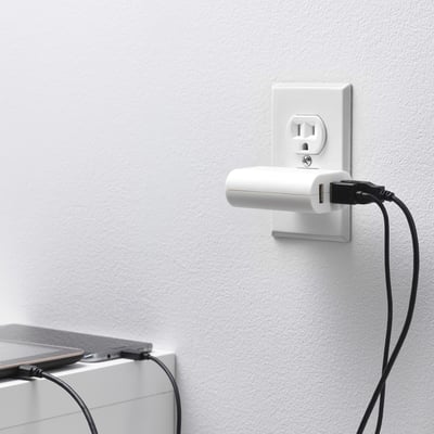 A compact, wall-mounted charger with three usb ports, plugged into an outlet, charging multiple devices.