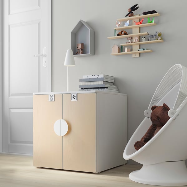 Modern kids room with light wood cabinet, white rocker, and shelves filled with toys and books.