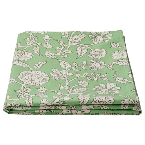 A folded green SMÖRFISK tablecloth with white floral designs and green leaves. Its made of 100% cotton, uniquely patterned, and rectangular.