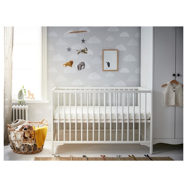 Baby room with white SOLGUL cot, cloud wallpaper, mobile, basket, and rug.