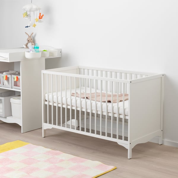 White baby cot with bevelled edges, two height settings, and a vented base. Fits next to a changing table with storage and toys.