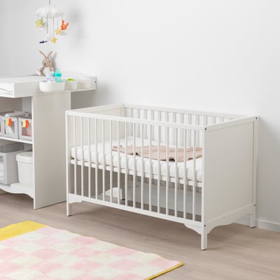 White baby cot with bevelled edges, two height settings, and a vented base. Fits next to a changing table with storage and toys.