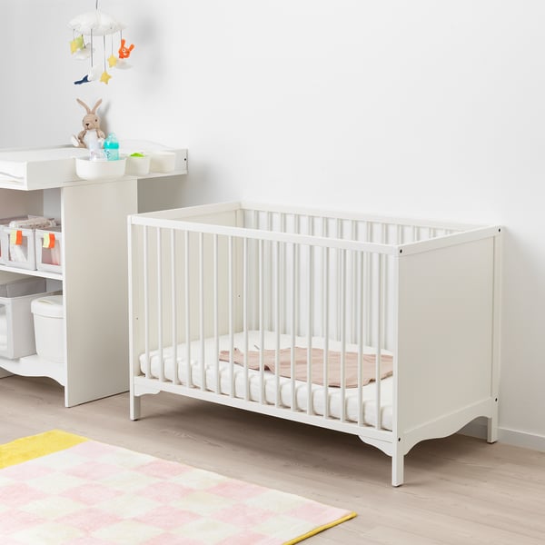 White crib on striped rug, with dresser and mobile.