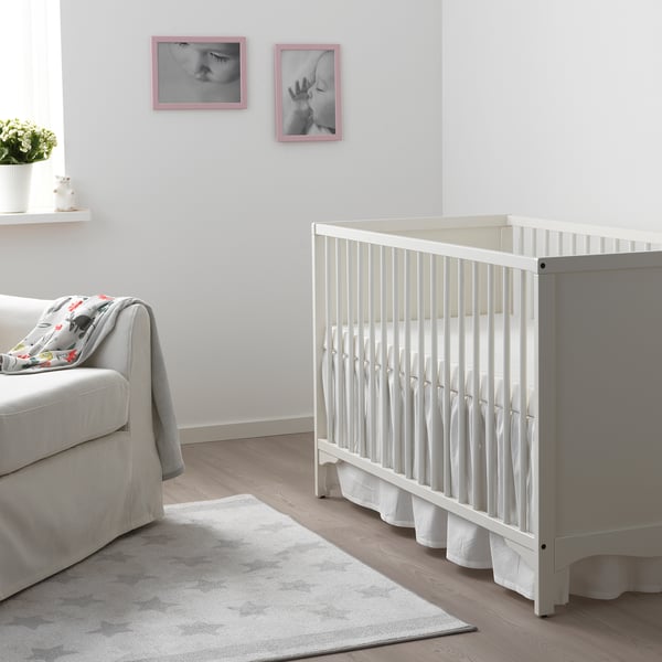 SOLGUL cot in nursery, next to grey armchair, under baby pictures, on light grey rug.
