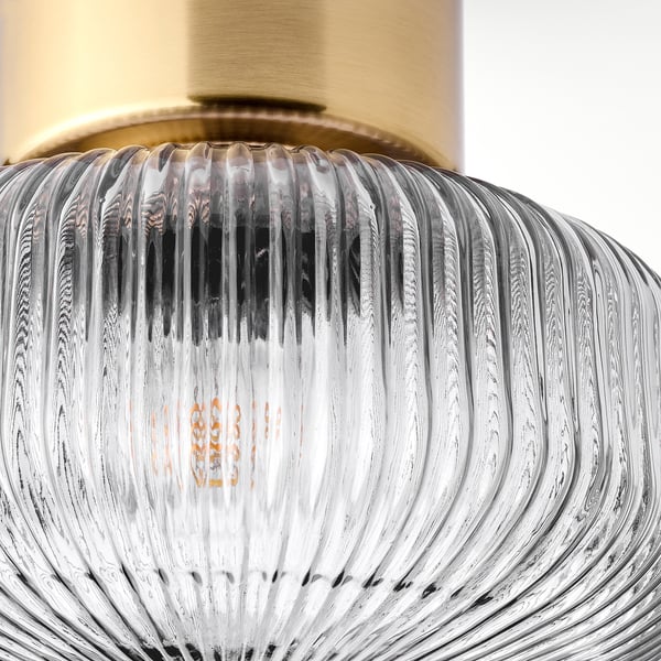 Clear glass lamp with rippled design, gold-topped, emitting warm light, exuding elegance.