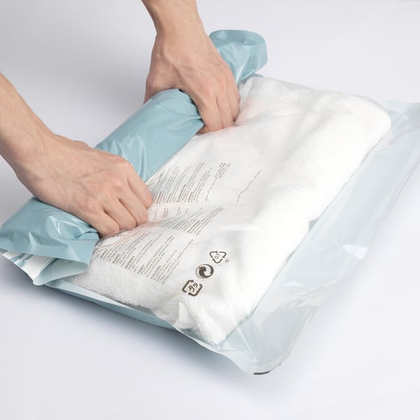 Person opening large blue SPANTAD vacuum bag, revealing rolled-up contents.