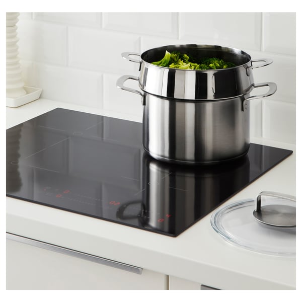 Stainless steamer on stove with green veggies.