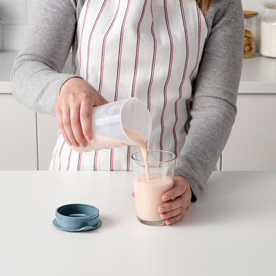 Person pours liquid from a measuring shaker into a glass on a kitchen counter.