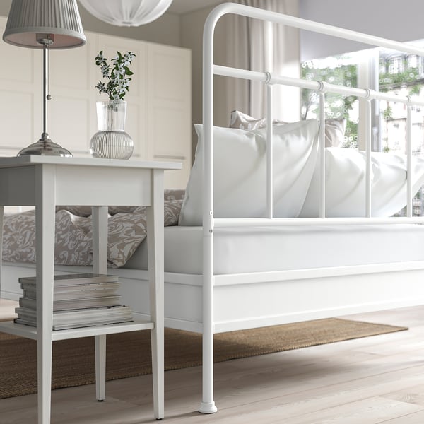 White bed with curved headboard, bedside table with books, lamp, and plant.
