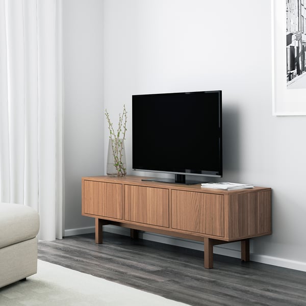 Modern tv stand STOCKHOLM in walnut, 3 cabinets, flat-screen tv, white wall, minimalist design, vase with branches, light-colored sofa.