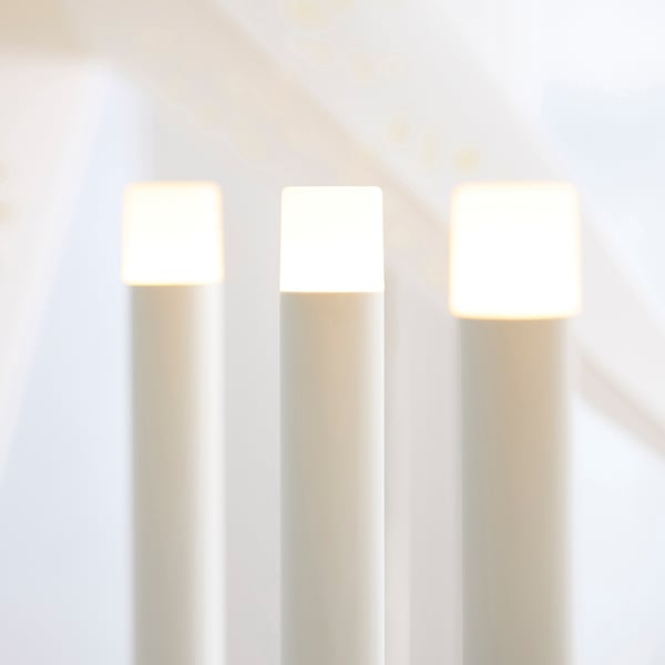 Three modern battery-powered led candles on stands, emitting warm light, arranged neatly on a reflective surface.