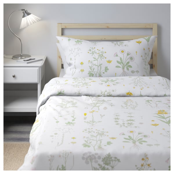 Cosy bedroom with white floral STRANDKRYPA duvet, wooden bed, small bedside table, and grey wall.