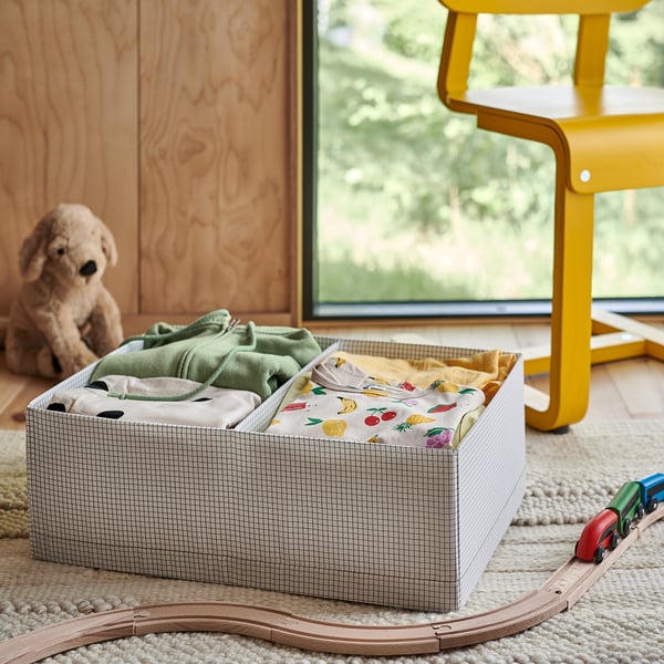 Box with grid pattern filled with clothes next to toy train on rug.