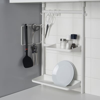 Kitchen hanging organiser with utensils on hooks and a shelf with a lid, against a tiled wall.