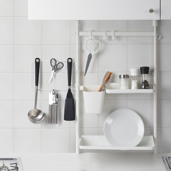 Organised kitchen storage. Utensils hang from clips, shelf holds plates and containers. Space-saving, handy design.