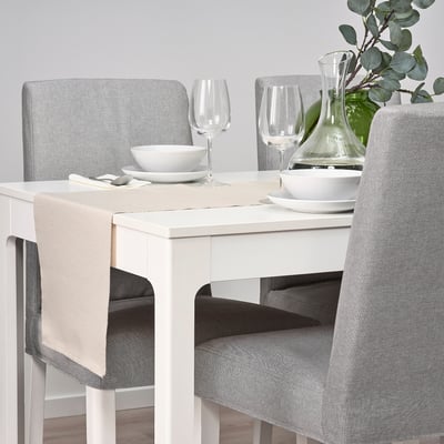 Table set with white dishes, glasses, and pitcher; grey chairs and beige table runner.