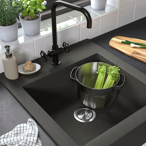 Dark grey farmhouse sink with high tap, filled with veggies in colander.